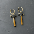 A pair of charcoal and tan enamelled brass claw hammer charm earrings on dark slate