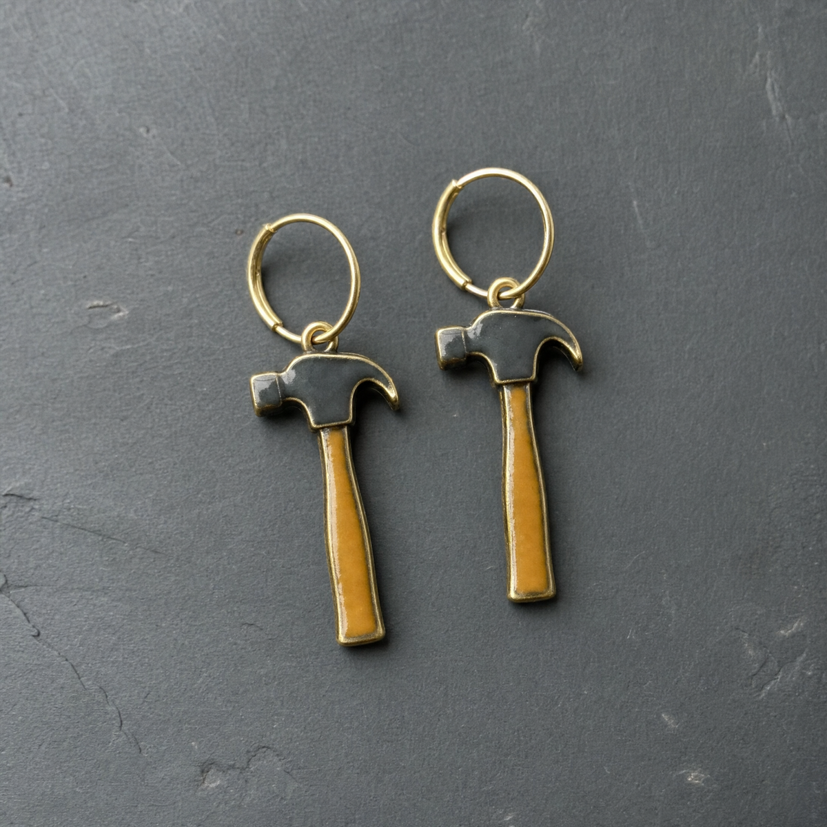 A pair of charcoal and tan enamelled brass claw hammer charm earrings on dark slate