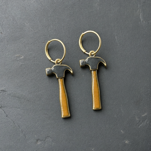 A pair of charcoal and tan enamelled brass claw hammer charm earrings on dark slate