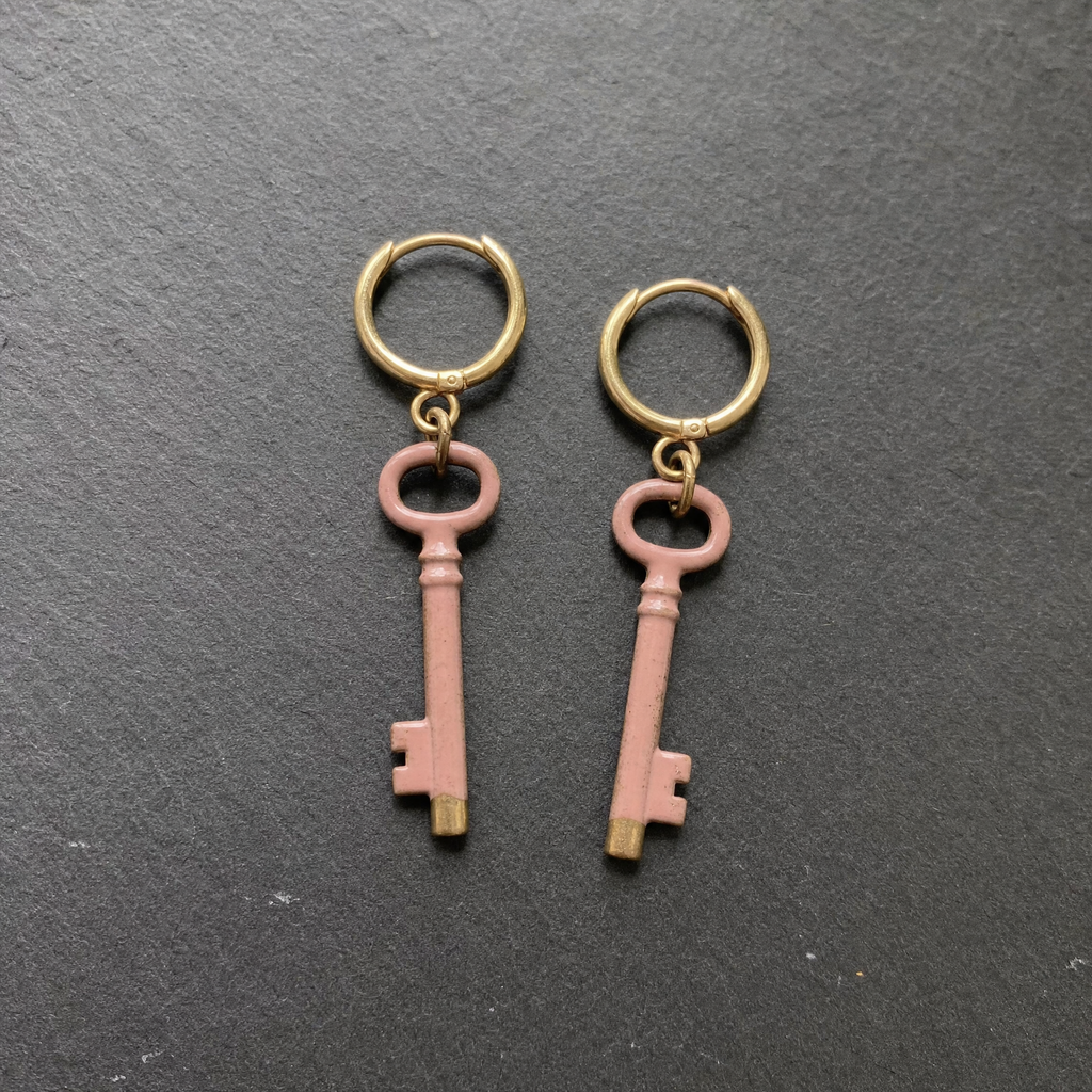 A pair of dusty rose enamelled brass key charm earrings on dark slate