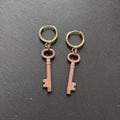 A pair of dusty rose enamelled brass key charm earrings on dark slate