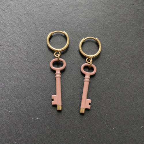 A pair of dusty rose enamelled brass key charm earrings on dark slate
