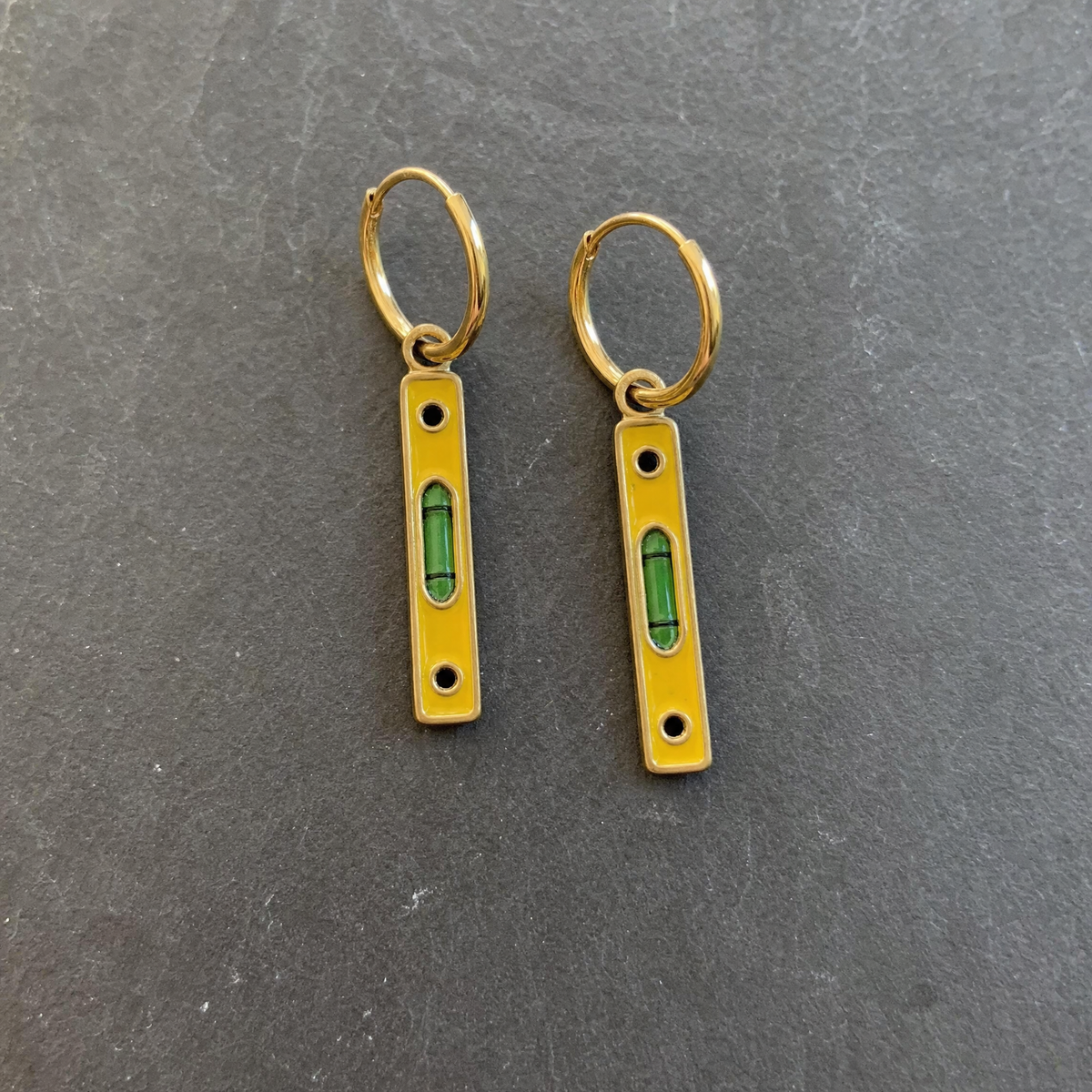 A pair of mustard enamelled brass spirit level charm earrings on dark slate