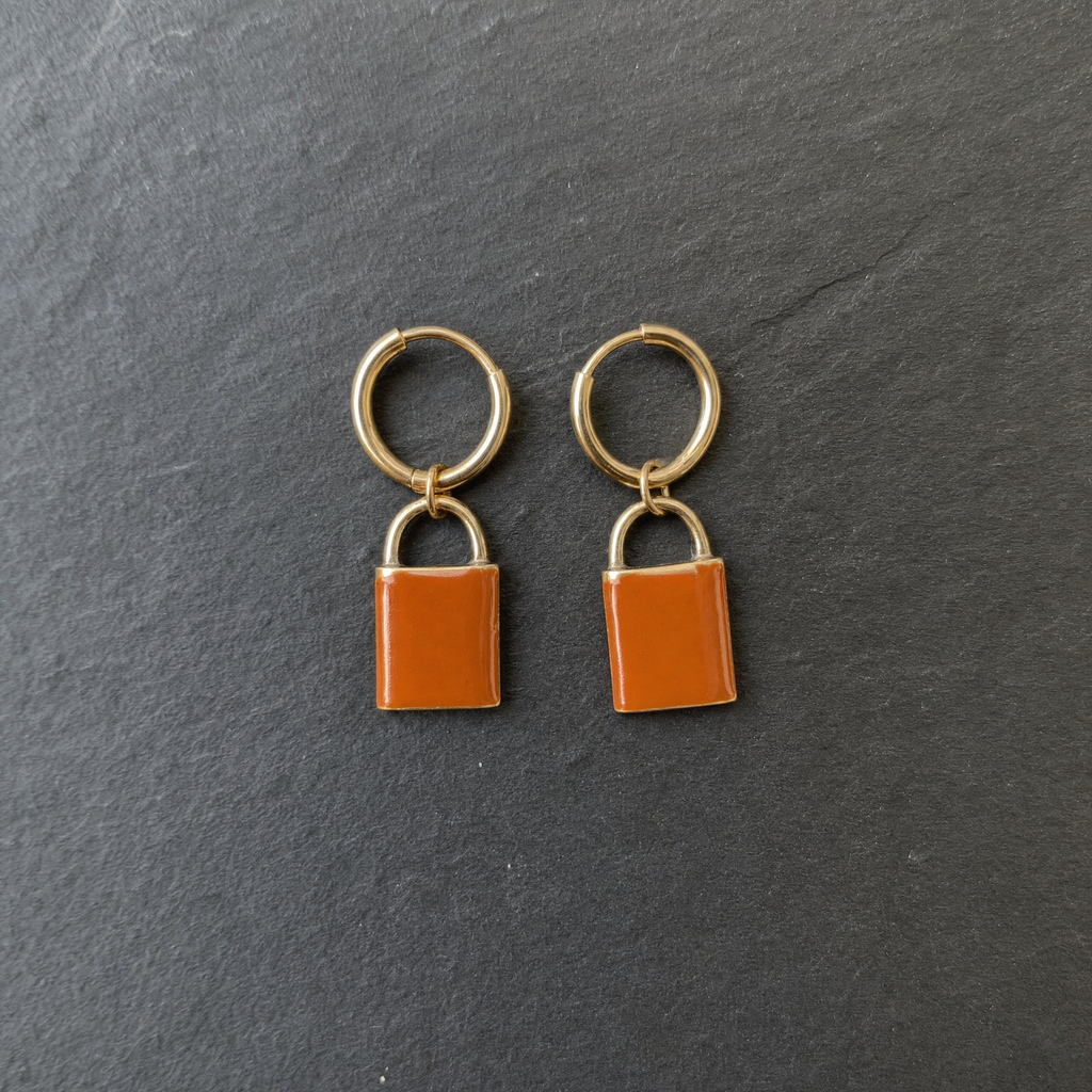 A pair of burnt orange enamelled brass padlock charm earrings on dark slate