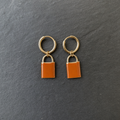 A pair of burnt orange enamelled brass padlock charm earrings on dark slate