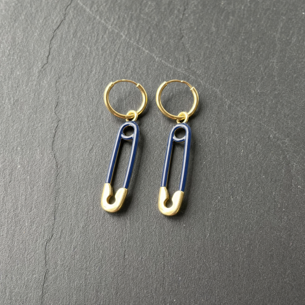 A pair of navy enamelled brass safety pin charm earrings on dark slate