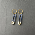 A pair of navy enamelled brass safety pin charm earrings on dark slate