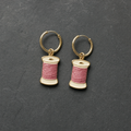 A pair of cream and dusty rose enamelled brass thread spool charm earrings on dark slate