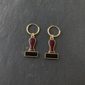 A pair of burgundy and black enamelled brass rubber stamp charm earrings on dark slate