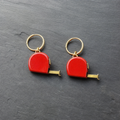 A pair of red enamelled brass tape measure charm earrings on dark slate
