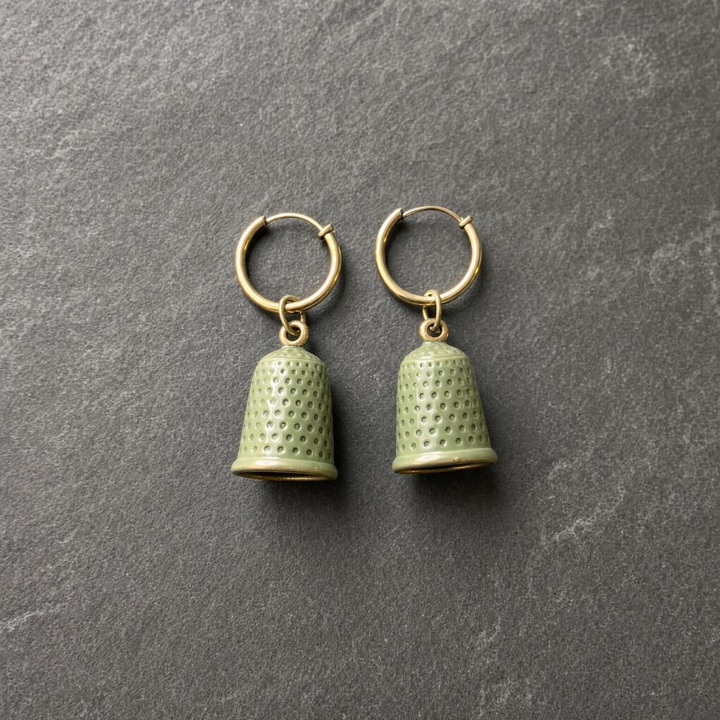 A pair of sage green enamelled brass thimble charm earrings on brass hoops, on dark slate