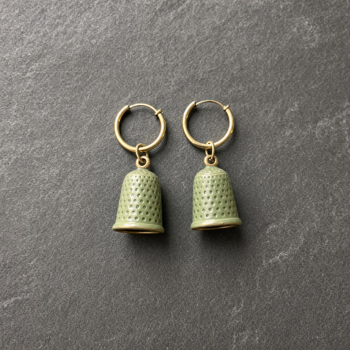 A pair of sage green enamelled brass thimble charm earrings on brass hoops, on dark slate