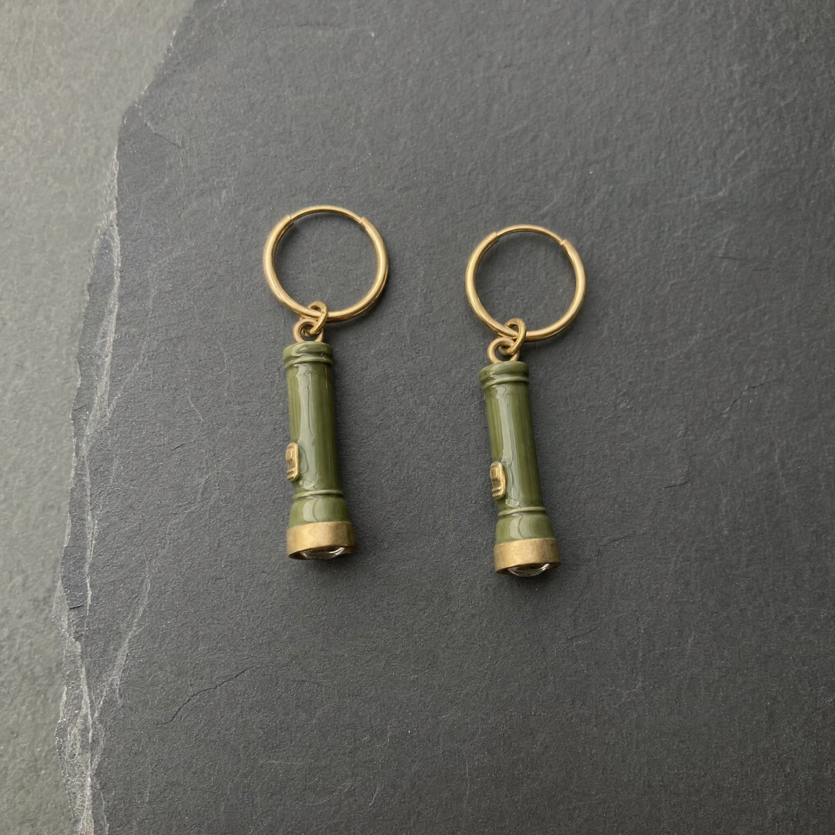 A pair of olive green enamelled brass pocket torch charm earrings on dark slate
